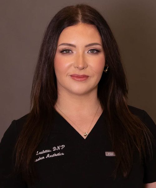 Headshot of a woman in black medical scrubs with long dark hair and light makeup against neutral background