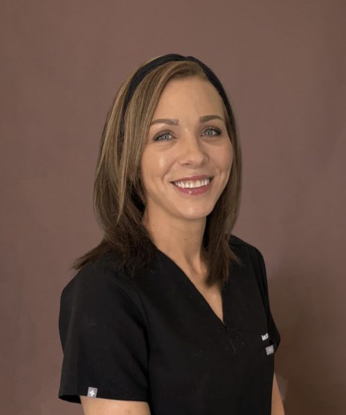 A smiling woman in black medical scrubs with a headband against a brown background.