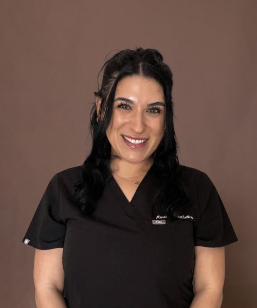 A smiling woman in black medical scrubs in front of a brown backdrop, professional headshot