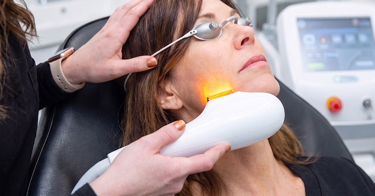 A woman receiving laser skin treatment on her neck wearing protective eye shields in a clinic