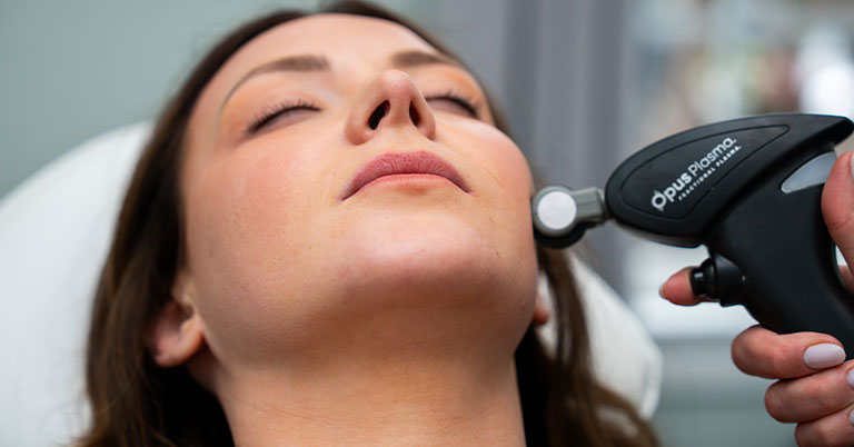 Woman reclined receiving Opus Plasma skin treatment on jawline with a handheld device