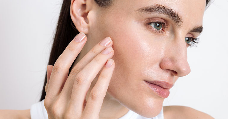 Close-up of a woman touching her cheek, showcasing glowing, healthy skin and natural makeup for skincare