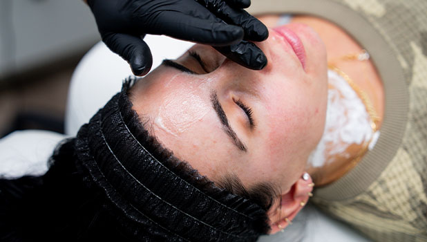 Woman receiving a facial treatment as an esthetician in gloves applies a mask to her forehead