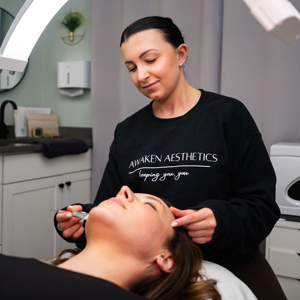 A woman aesthetician performing a facial treatment on a reclining client in a skincare clinic