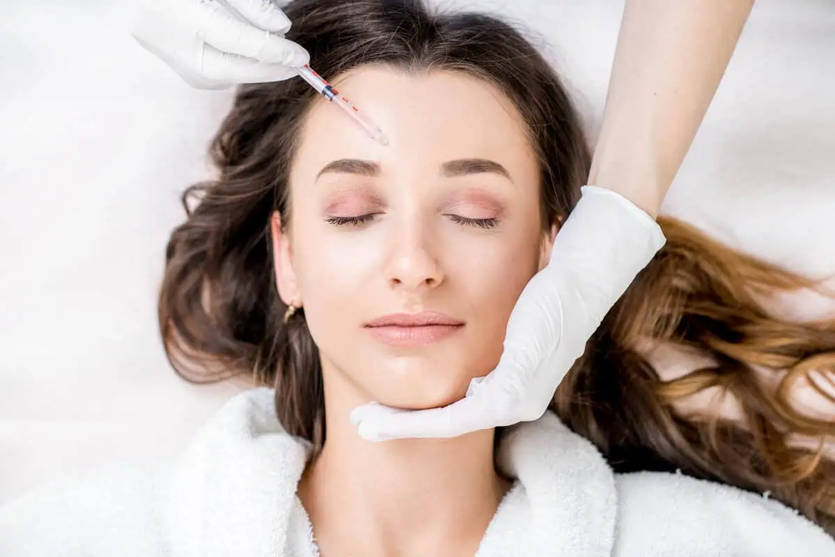 A woman receiving a cosmetic Botox injection to her forehead at a clinic, clinician in gloves supports her chin