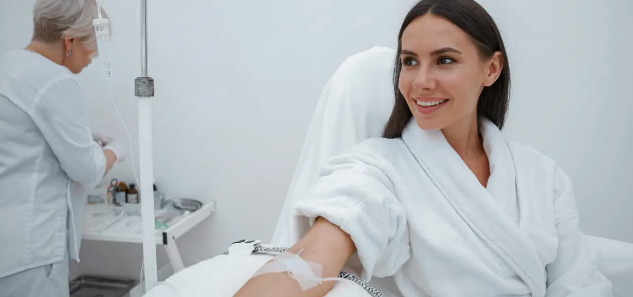 Smiling woman in a white robe receiving IV infusion in a bright medical spa treatment room