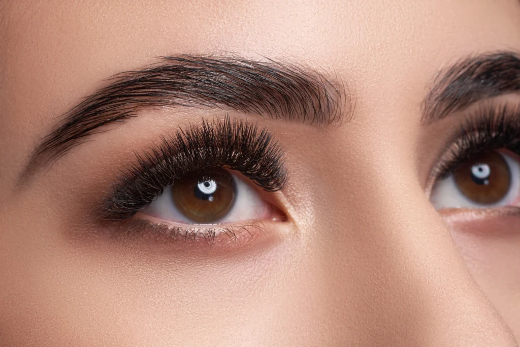 Close-up of a woman's brown eyes with long eyelash extensions, groomed eyebrows and soft neutral eye makeup.