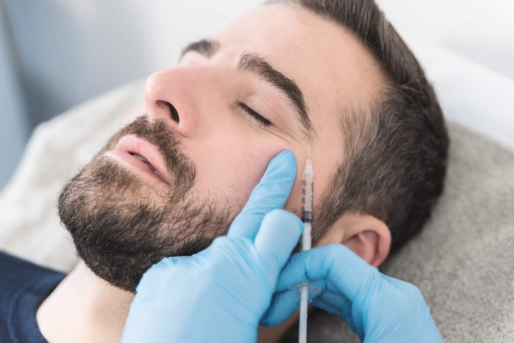 Close-up of a man receiving a cosmetic cheek injection from a clinician wearing blue gloves.