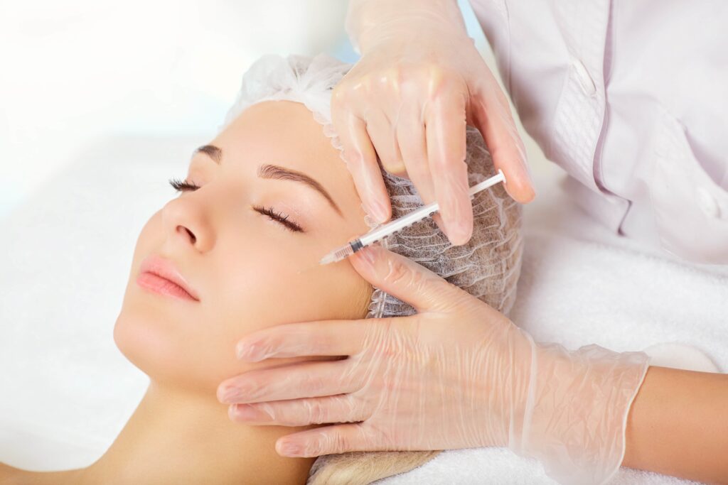 A woman receiving a cosmetic facial injection near the cheek from a practitioner wearing gloves in a clinic.