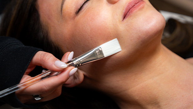 Close-up of a woman receiving a facial treatment while a brush applies a mask to her chin